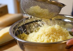 Проціджування тертої картоплі через сито для видалення зайвого соку під час підготовки маси для дерунів.