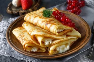 Готові млинці з сиром, подані зі сметаною та ягодами