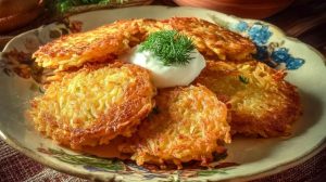 Готові хрусткі деруни подані на тарілці зі сметаною та свіжим кропом — традиційна українська подача.