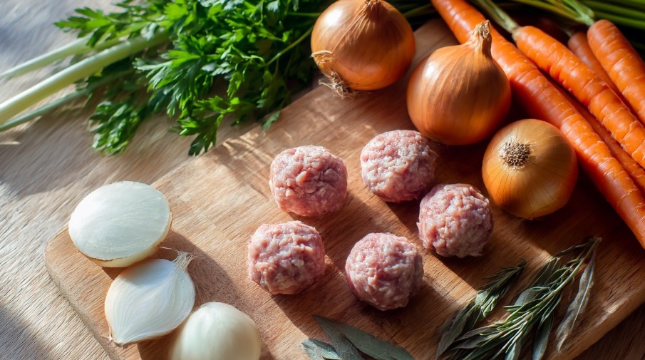 Овочі для супу та фрикадельки на дерев’яній дошці